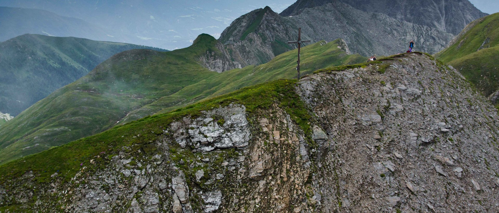 Vzhůru na Wilde Kreuzspitze! A mountainous landscape with stones and meadows. In the background you can see more mountains and a partly cloudy sky